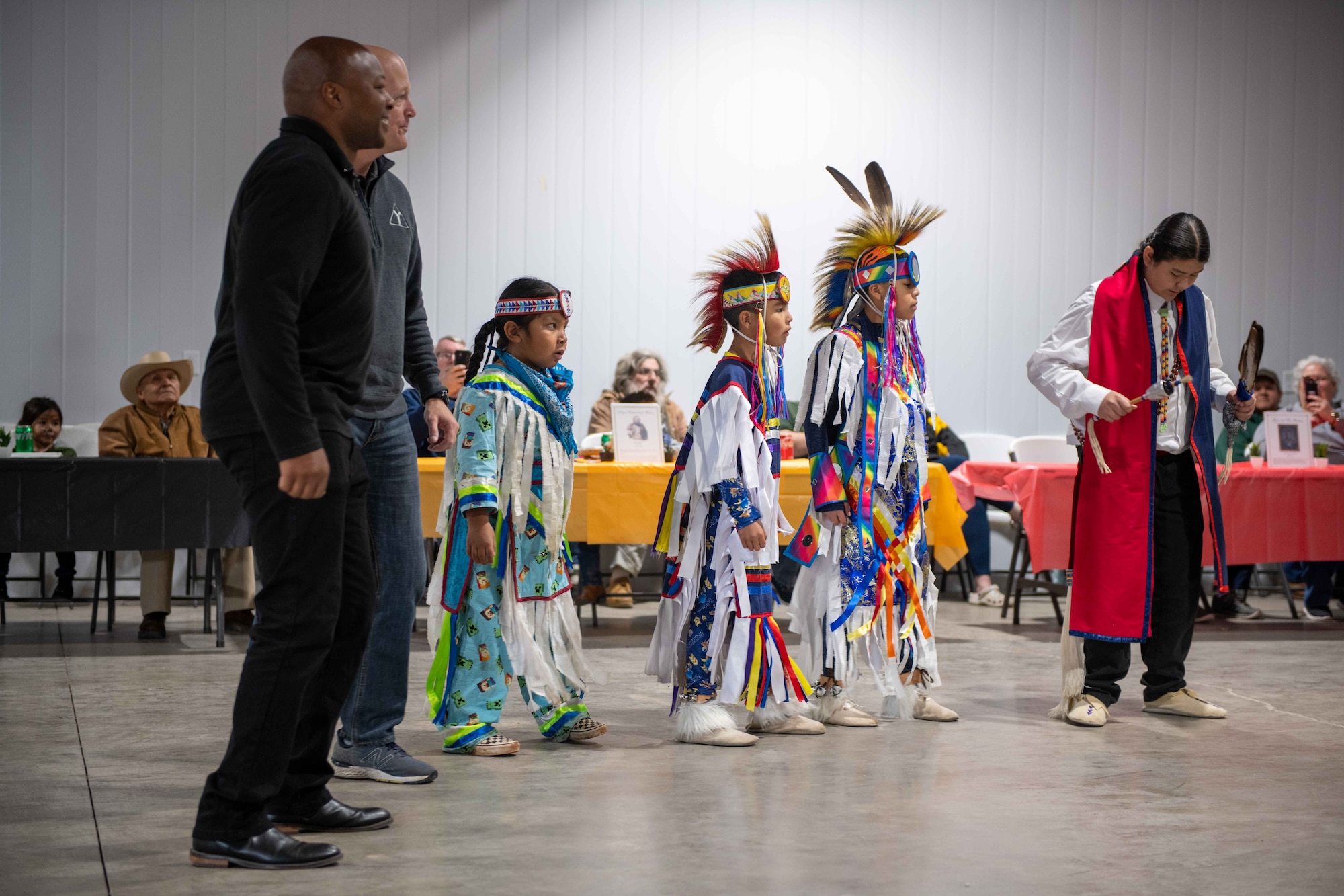 From the left, Col. Patrick Brady-Lee, 97th Air Mobility Wing vice commander, and Col. Blaine Baker, 97th AMW commander, perform with the Comanche Nation Youth Dancers around the Jackson County Expo Center, Nov. 19, 2022, in Altus, Oklahoma. Baker later awarded Teresa Lopez, coordinator for the Comanche Nation Youth Dancers, with a 97 AMW commander’s coin.(U.S. Air Force photo by Airman 1st Class Kari Degraffenreed)