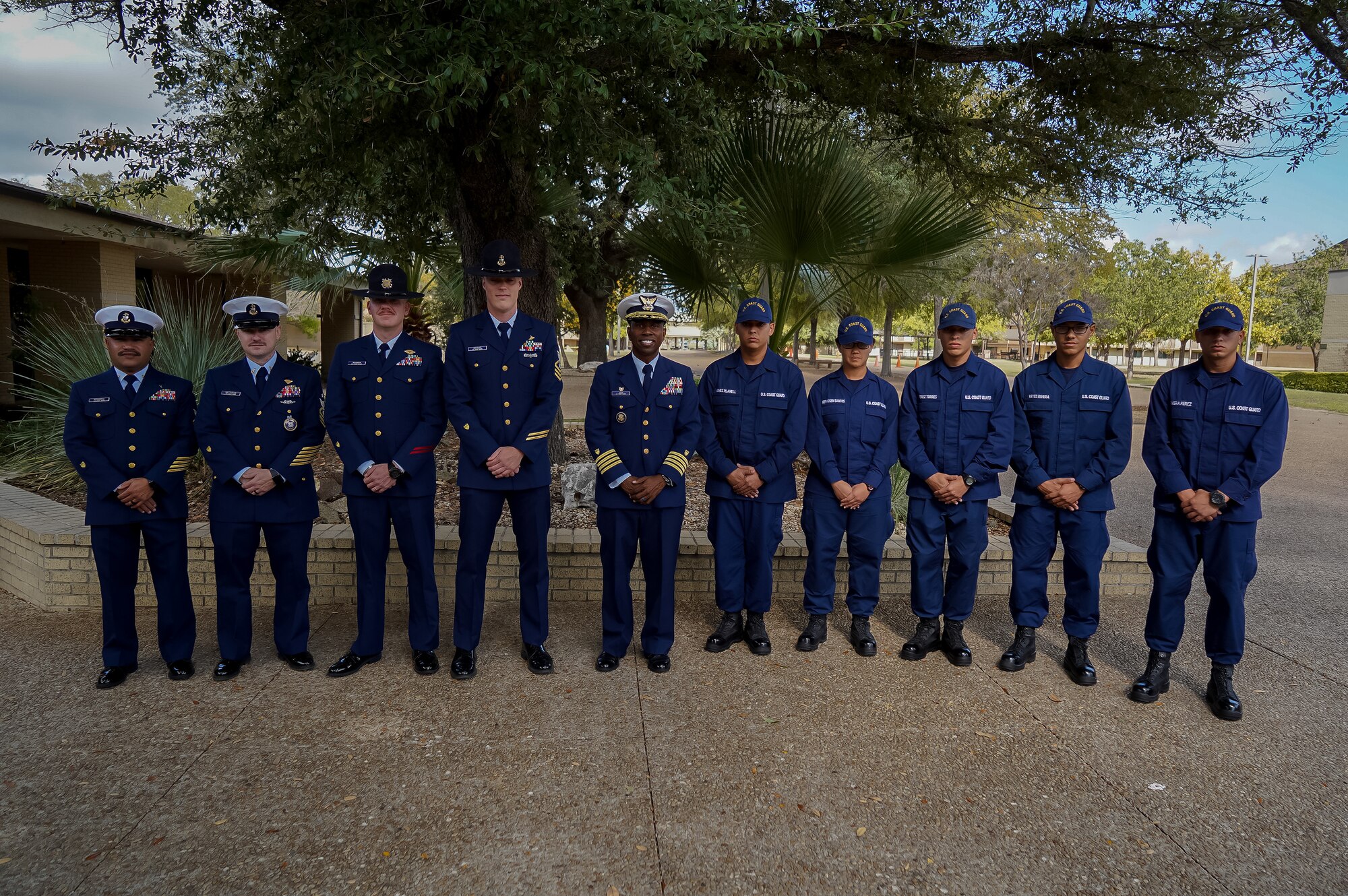 A group of people dressed in a dark blue Coast Guard uniform stand side by side posing for the camera. It is a full body shot.