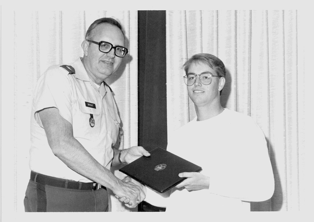 Black and white photo of a man in uniform presenting award to young man in glasses.