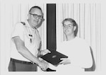 Black and white photo of a man in uniform presenting award to young man in glasses.