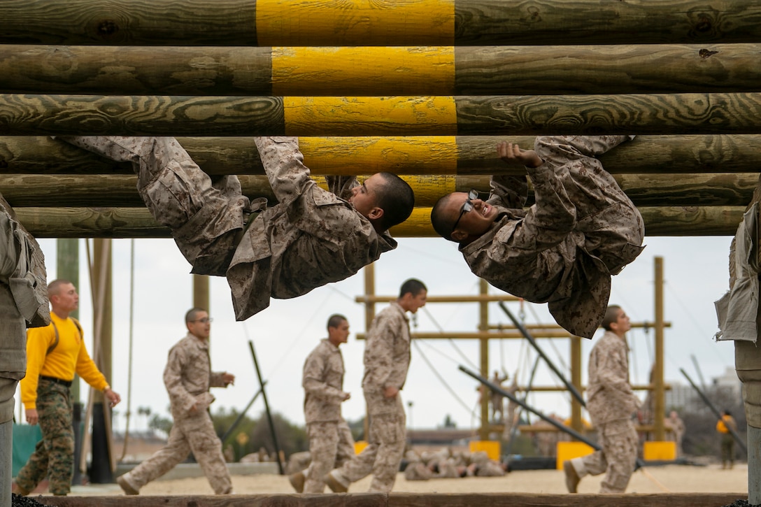 Two Marine Corps recruits climb across logs upside down as part of an obstacle course.