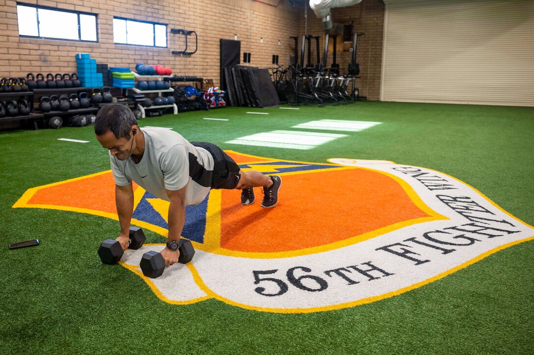 An airman performs a pushup with dumbbells.