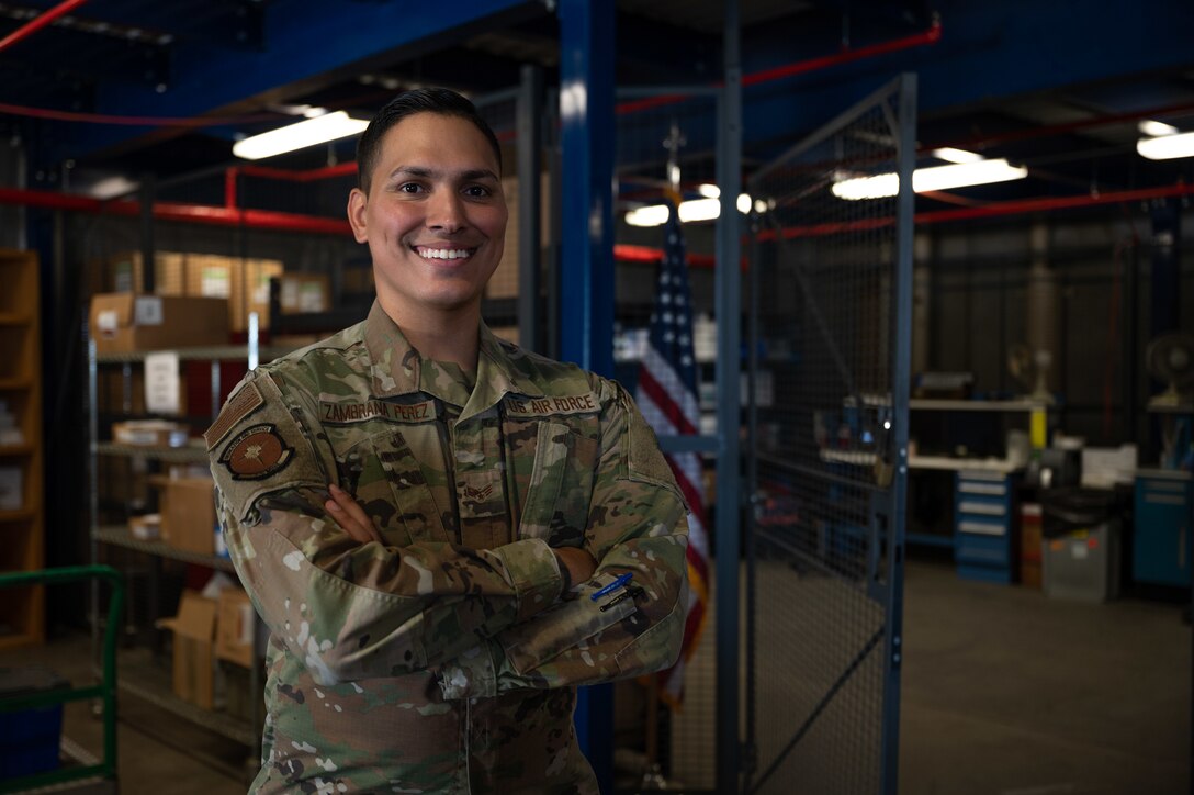 An Airman crosses his arms and smiles in a warehouse