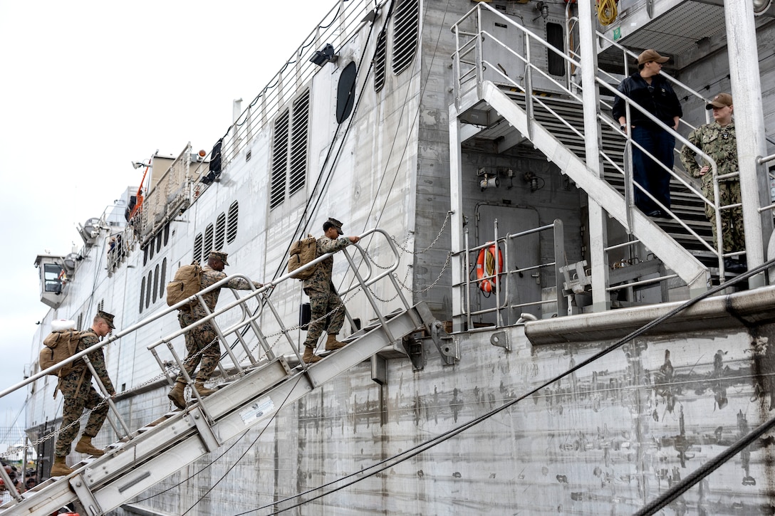 Three Marines with backpacks walk up a ramp to board a ship.