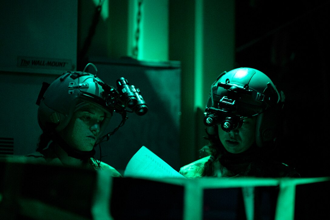 Two airmen wearing night vision gear look at papers.