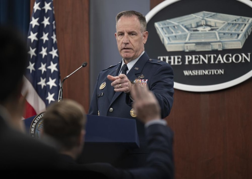 A man in a uniform at a lectern gestures towards an audience member. The sign behind him indicates that he is at the Pentagon.