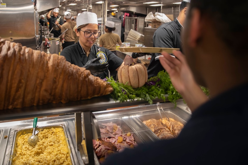 A server preps food at a serving station with various types of foods.