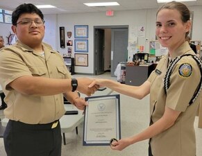 220905-N-LY580-1001 ALEXANDER CITY, Ala. (Sept. 4, 2022) Benjamin Russell High School Navy Junior Reserve Officers Training Corps Cadet Commanding Officer Courtney Burgess, right, presents Cadet Andrew Ramirez a Cadet of the Month certificate and command coin for earning the unit's Cadet of the Month for September 2022. (U.S. Navy photo by James Stockman)