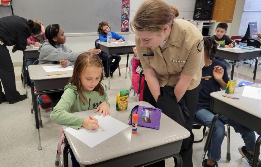 221019-N-LY580-1008 ALEXANDER CITY, Ala. (Oct. 19, 2022) Benjamin Russell High School Navy Junior Reserve Officer Training Corps Cadet Katherine Taylor, right, speaks with a second-grade student at Jim Pearson Elementary School during a book reading event to highlight the importance of reading. (U.S. Navy photo by James Stockman)