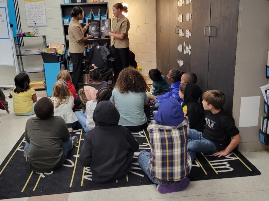 221019-N-LY580-1001 ALEXANDER CITY, Ala. (Oct. 19, 2022) Benjamin Russell High School Navy Junior Reserve Officer Training Corps Cadets Monce Santiago, left, and Natalie Brown read a book to second-grade students at Jim Pearson Elementary School during a book reading event to highlight the importance of reading. (U.S. Navy photo by James Stockman)