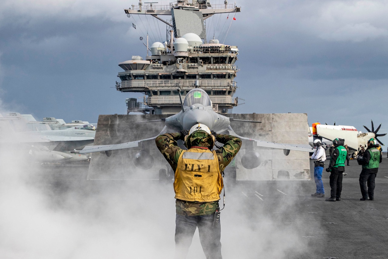 Sailor on a ship’s flight deck directs a jet pilot.