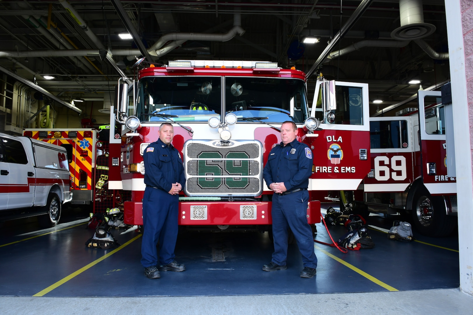 two firefighters in dress uniforms in front of a fire engine