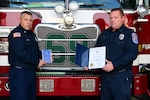two men holding awards in front of a fire engine