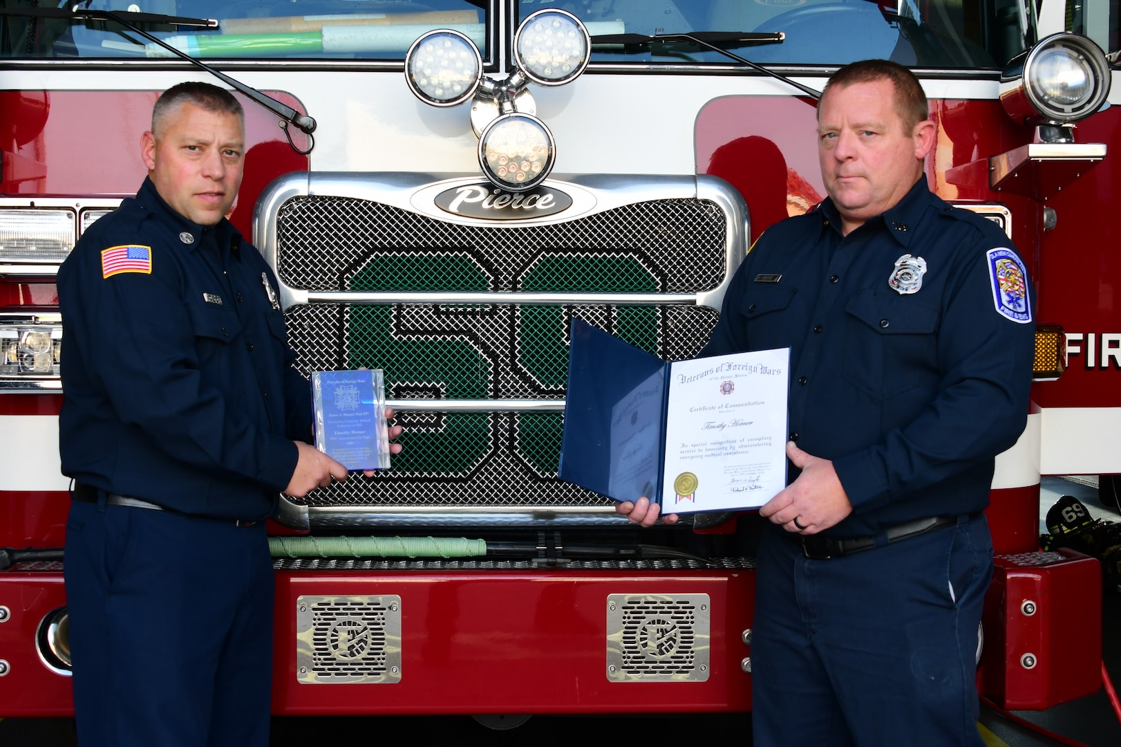 two men holding awards in front of a fire engine