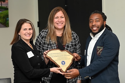 3 people smile while holding an award