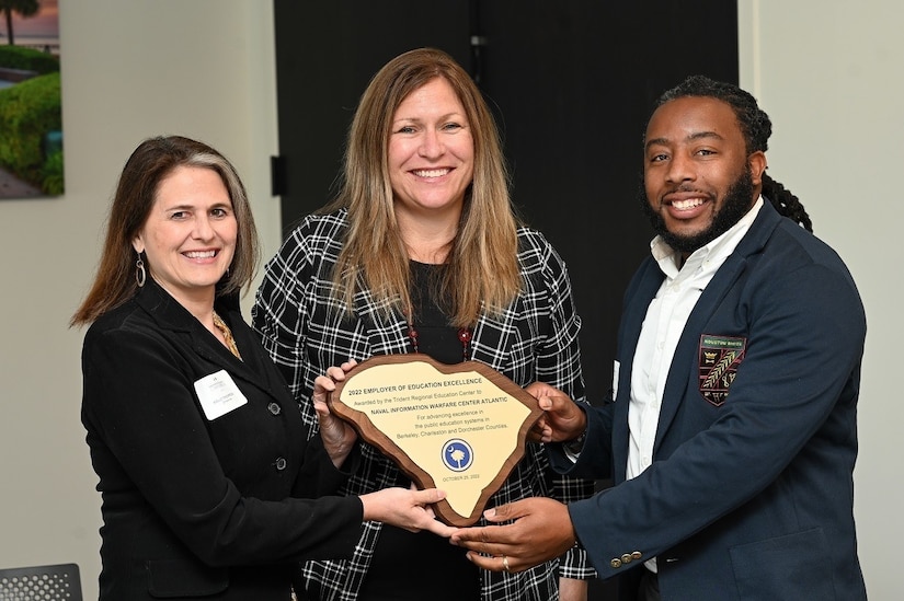 3 people smile while holding an award