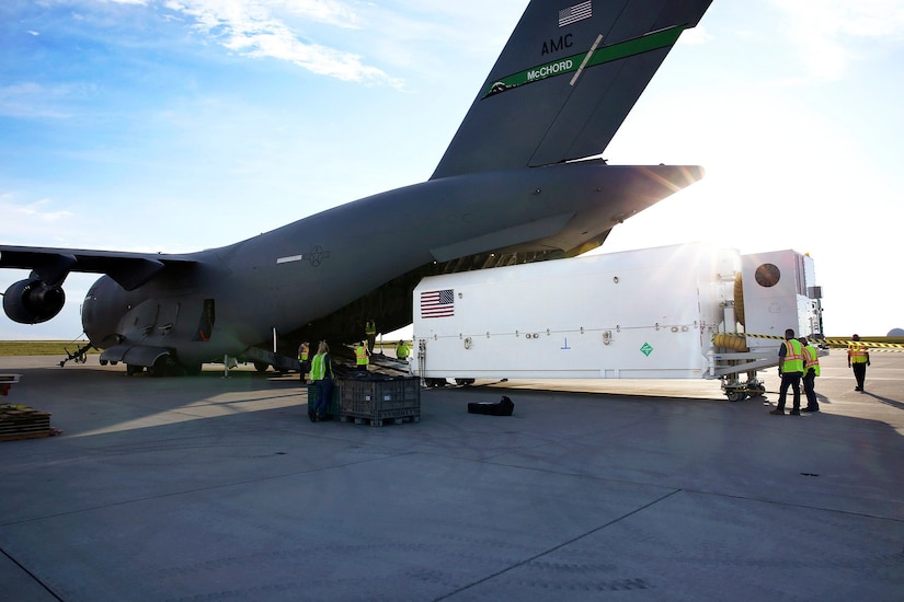 Personnel load a  satellite onto an aircraft.