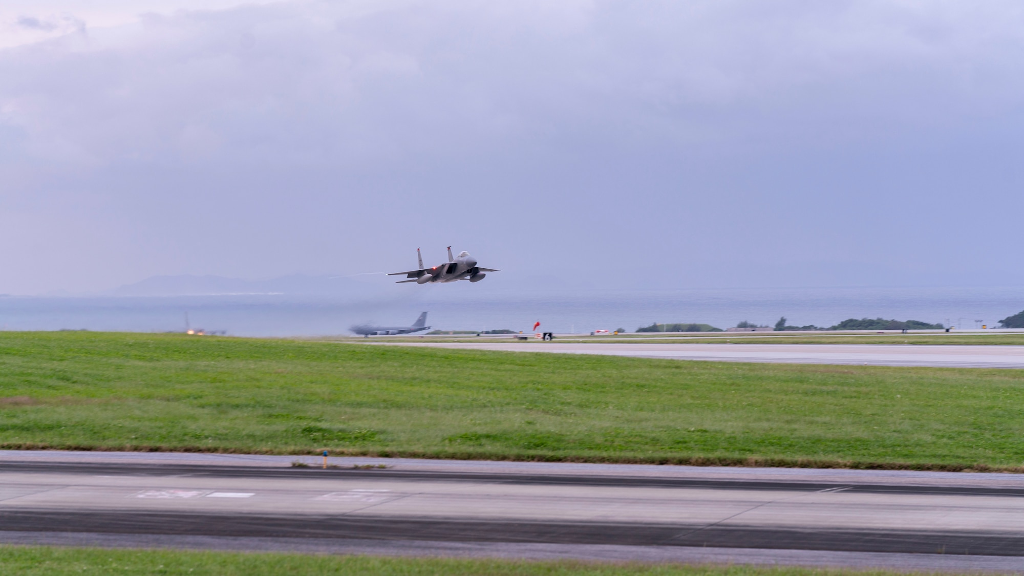A grey Air Force F-15 takes off over a landing strip at Kadena Air Base
