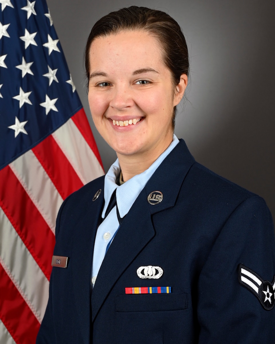 Official bio photo of A1C Eliza Edge in front of the American flag. She is wearing the blue service dress uniform.