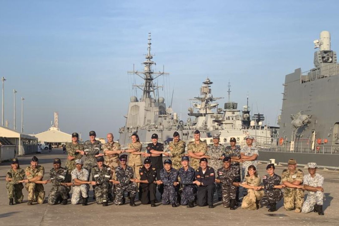 A large group of service members pose for a photo in front of a ship.