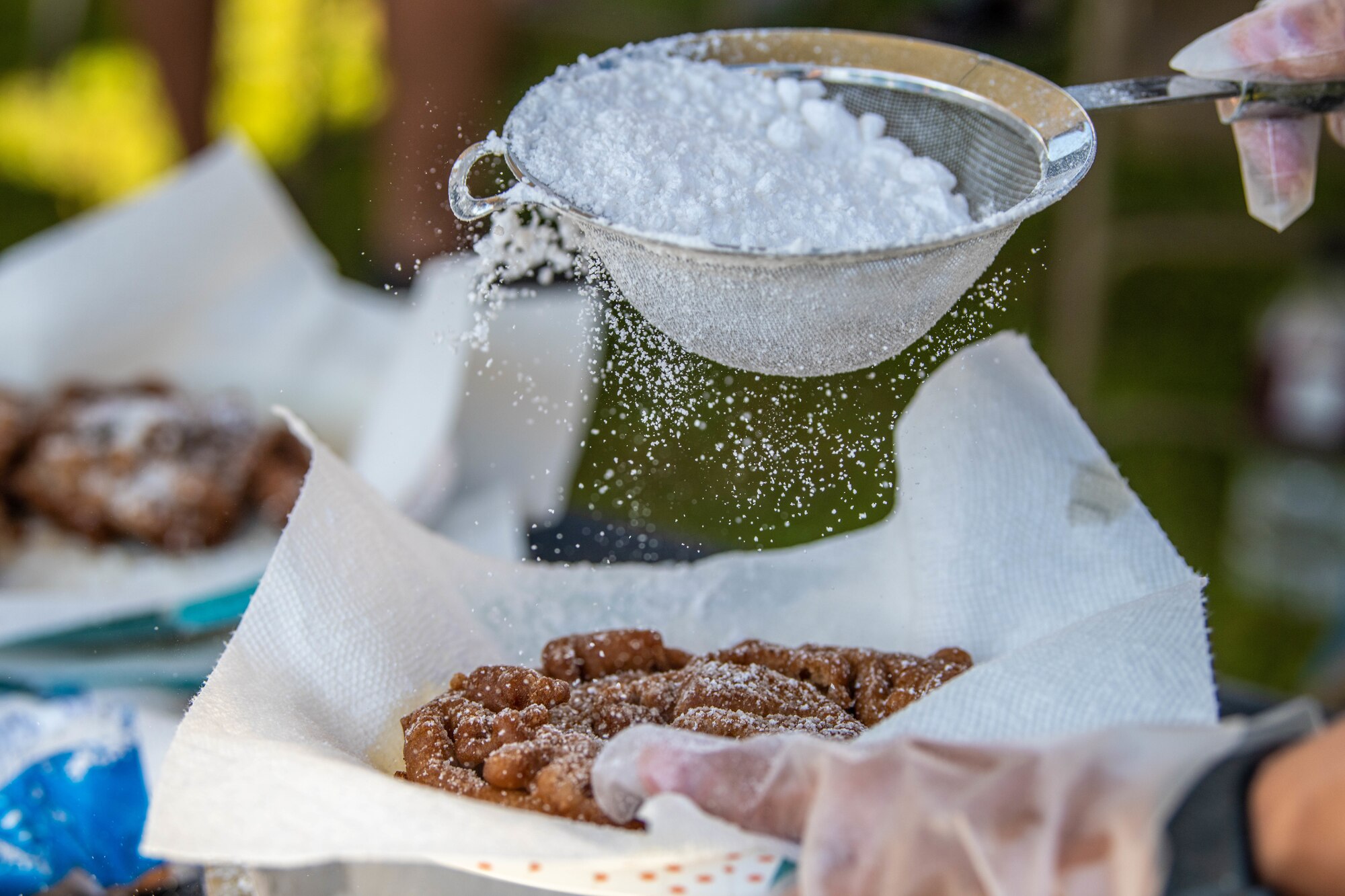 A food vendor sprinkles powdered sugar on top of a funnel cake