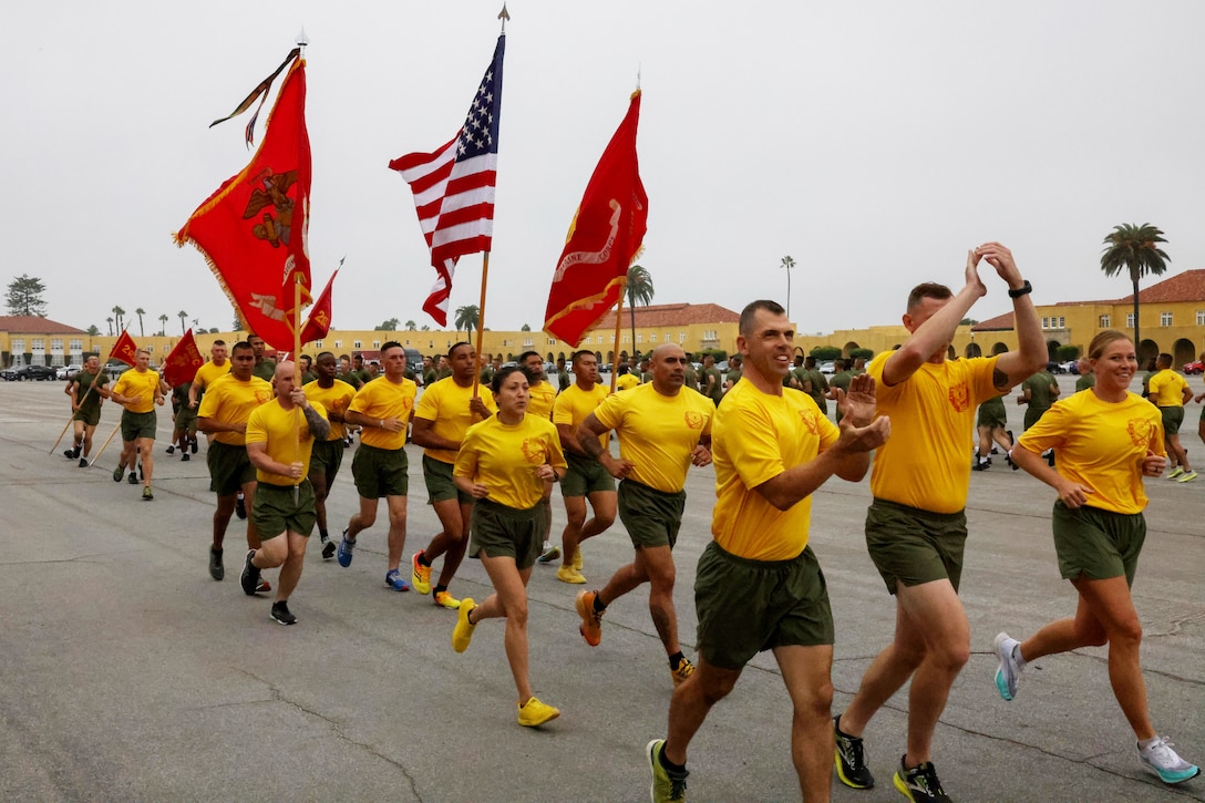 A group of Marines run together, some carry flags.