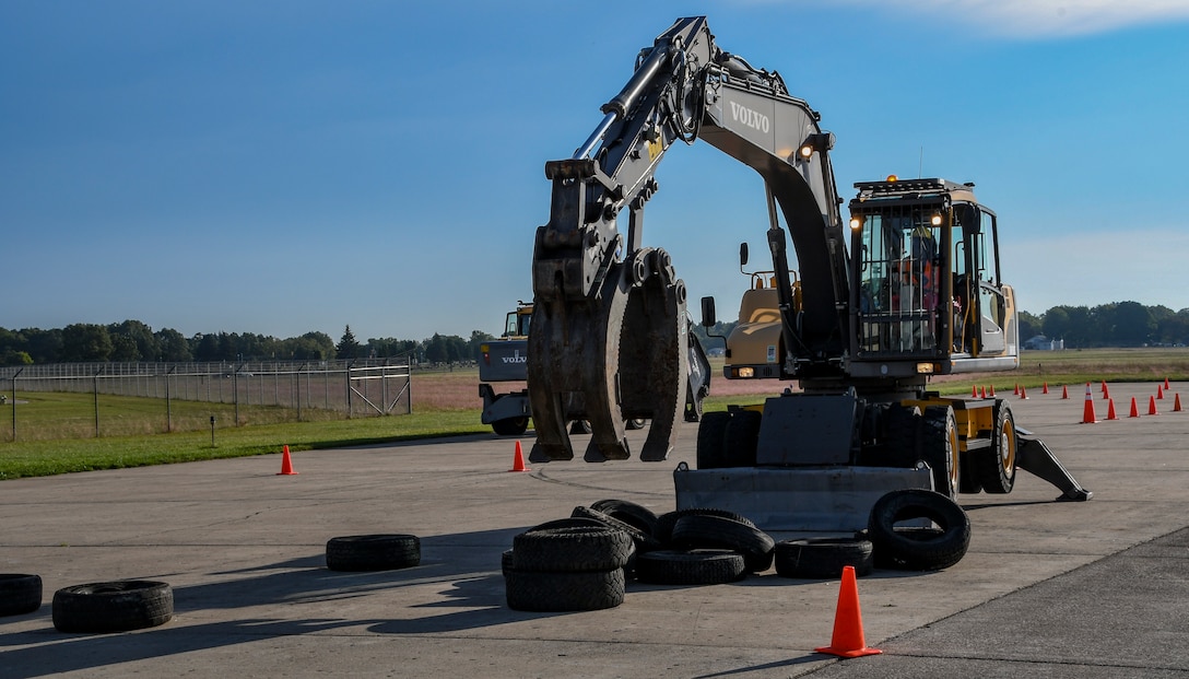 A large piece of with a grapple attachment on the boom arm stacks tires as part of the class.