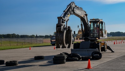 A large piece of with a grapple attachment on the boom arm stacks tires as part of the class.