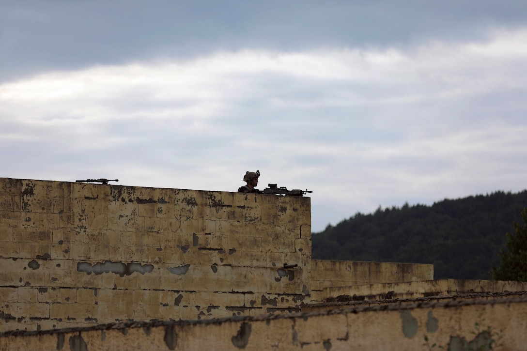 A soldier perches on a rooftop.