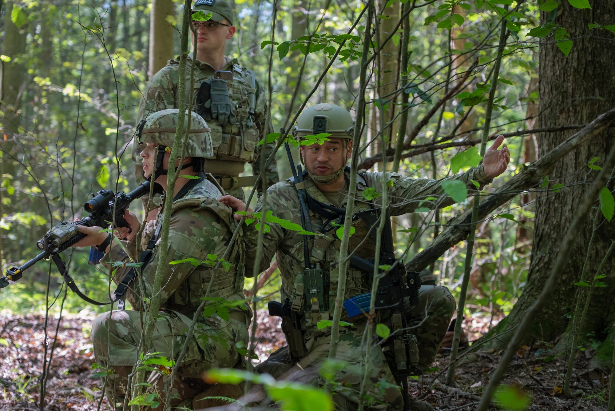 Three Airmen kneel in a forest.