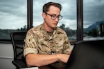 Man in United Kingdom military uniform wearing glasses, types on a laptop