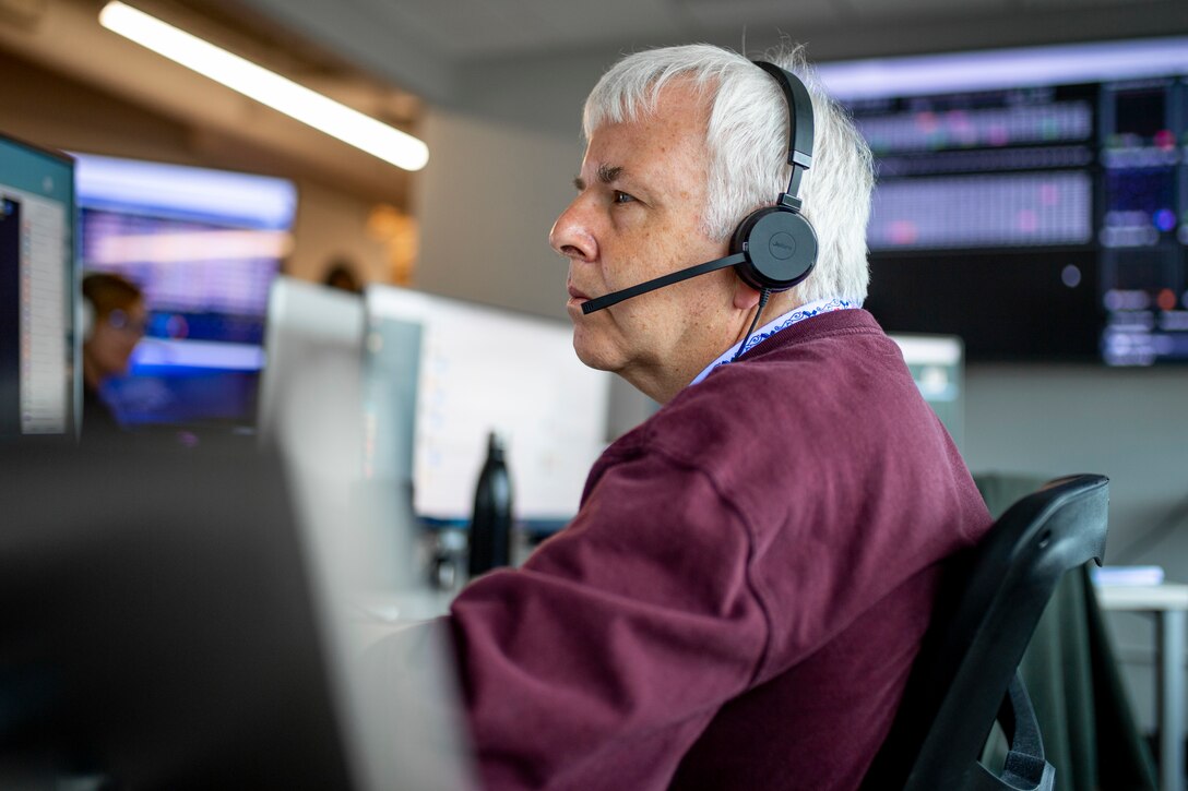 Man wearing headset looks at computer screens