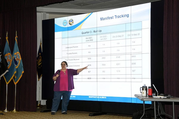 A woman presents in front of a large projection screen.