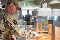 An Airman uses tongs to grab some fries from a buffet table.