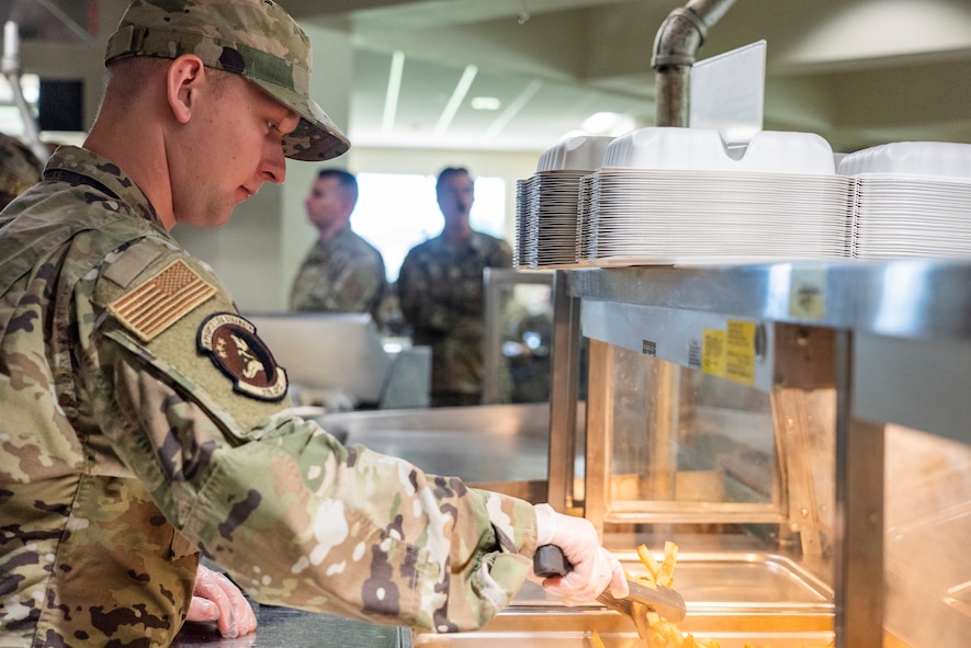 An Airman uses tongs to grab some fries from a buffet table.
