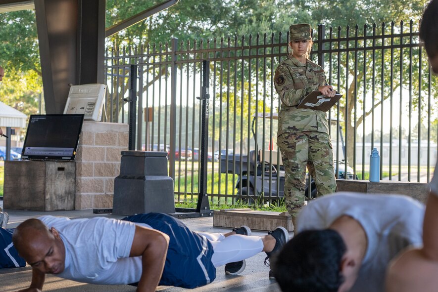 An Airman watches Airmen perform pushups.