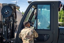 An Airman stands outside a forklift and talks to an Airman in protective gear sitting in the forklift.