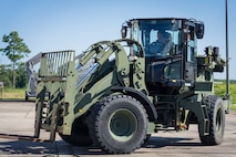 An Airman drives a forklift on pavement.