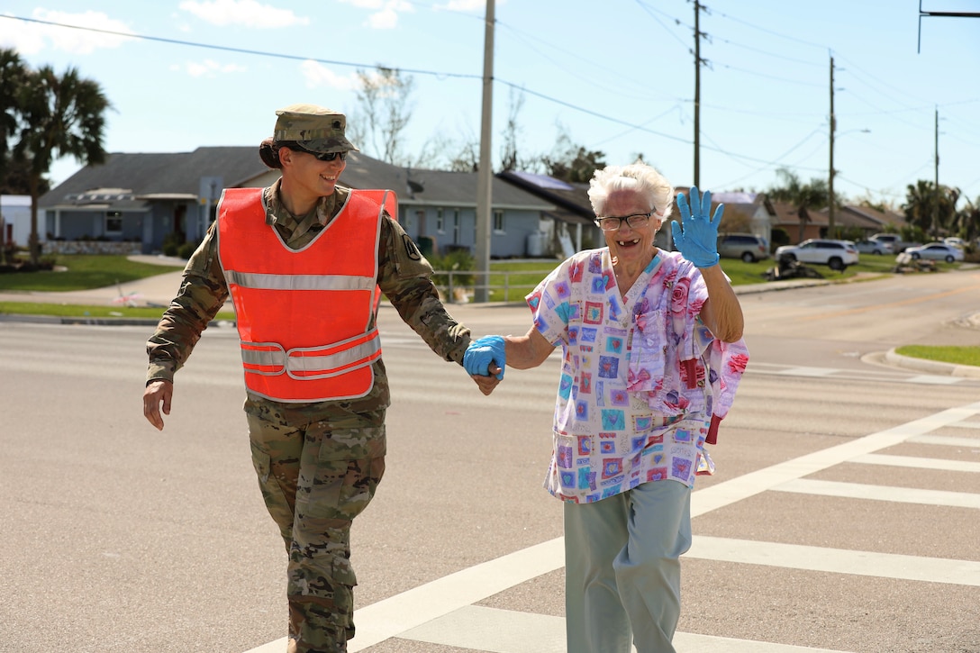 A soldier holds an elderly resident’s hand while helping her cross the street.
