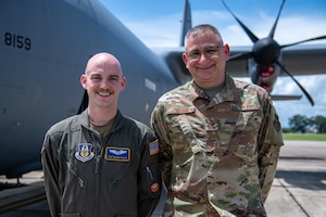 Two Airmen stand in front of a C-130J