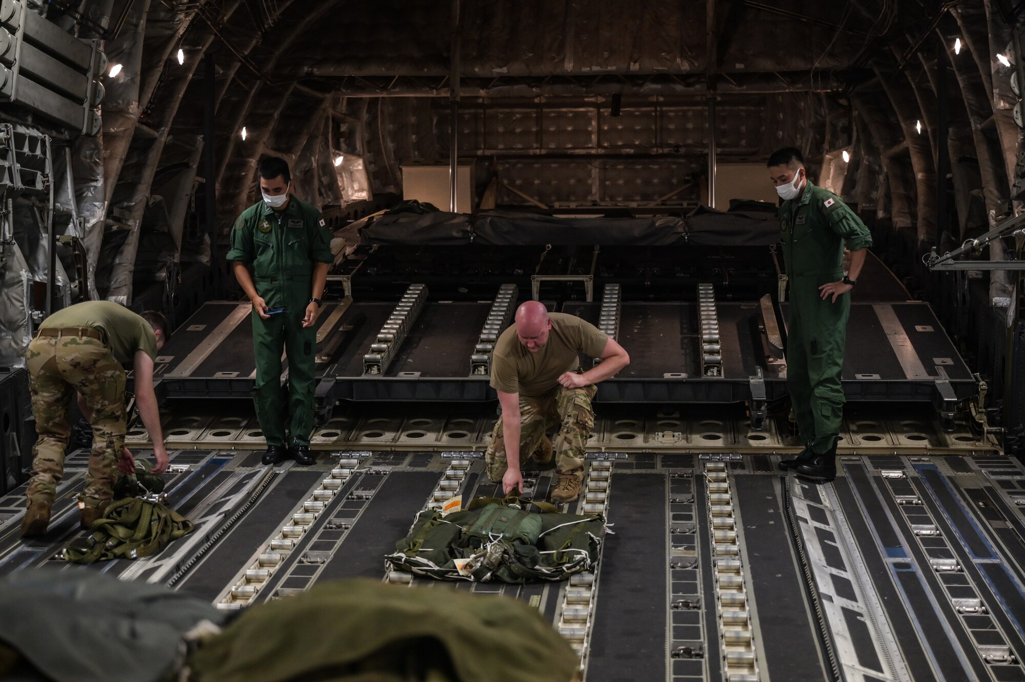 U.S. Air Force Senior Airman Andrew Girard, 535th Airlift Squadron loadmaster, and Staff Sgt. Jory Linneman, 15th Operations Support Squadron joint airdrop inspector, secure cargo parachutes inside a C-17 Globemaster III alongside Japan Air Self-Defense Force Senior Master Sgt. Kotaro Tanaka and Tech. Sgt. Katsuhiko Chikuma, 403rd Tactical Airlift Squadron loadmasters during a bilateral exercise at Joint Base Pearl Harbor-Hickam, Hawaii, Sept. 28, 2022. This is the first bilateral exercise between the squadrons, increasing interoperability and familiarizing both services with the capabilities of the Kawasaki C-2 and C-17. (U.S. Air Force photo by Staff Sgt. Alan Ricker)