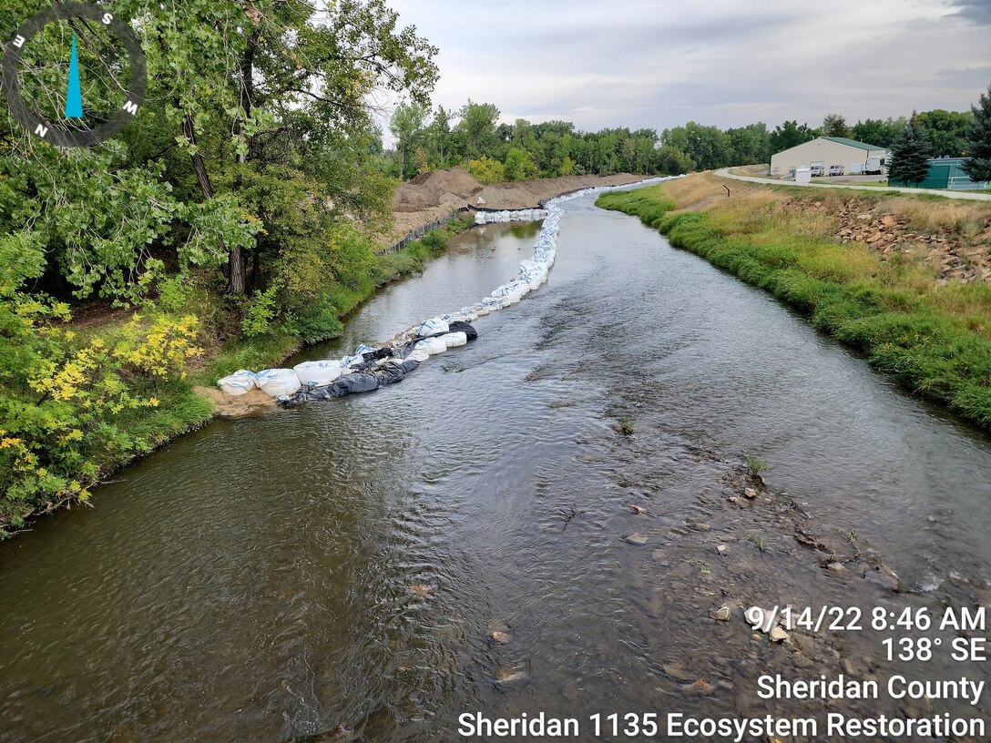 A photo of a creek with a large storage shed in the background