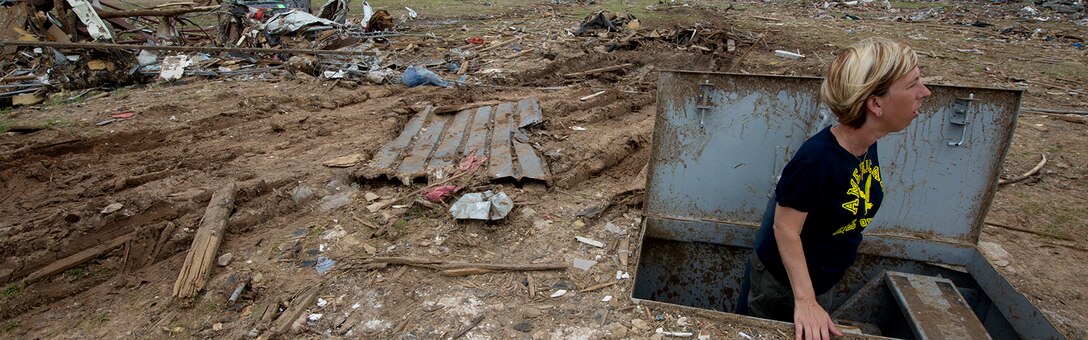 Christie England, an acquisition law paralegal with the 72nd Air Base Wing, Tinker Air Force Base, Okla., stands in her storm shelter in front of the remains of her home in Moore, Okla., May 27, 2013. England's home was destroyed in the May 20 EF-5 tornado that ripped through Moore. The storm killed 24, injured hundreds and damaged thousands of homes. England is from Olathe, Kan. (U.S. Air Force photo by Tech. Sgt. Bradley C. Church) Cropped version of 130527-F-IE715-189