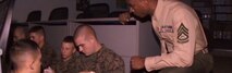 Frame from active shooter guidance video VIRIN 110126-D-#####-001 showing Marines sitting on the floor between desks and a Marine Corps leader kneeling with them to give instruction in a darkened classroom.