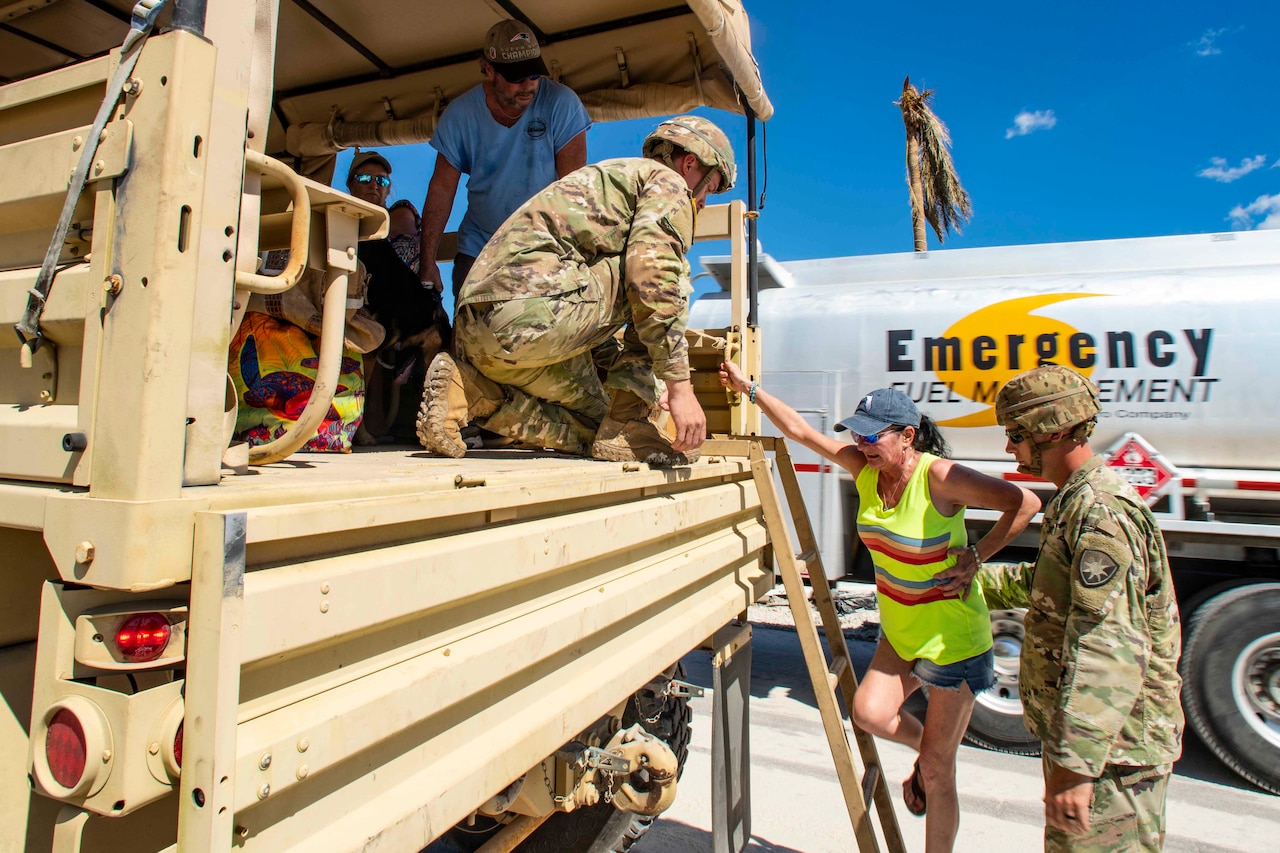 Guardsmen help a resident into a military vehicle.