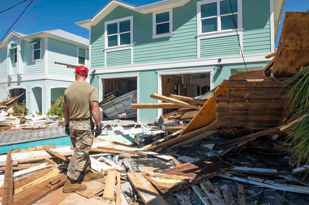 A guardsman walks through rubble toward a house that has debris spilling out.