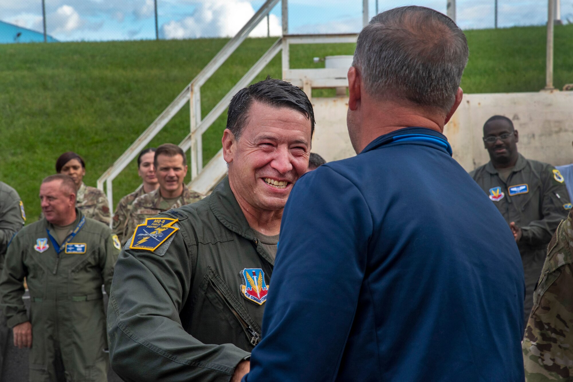 A man in a flight suit smiles while shaking hands with a man in civilian attire.