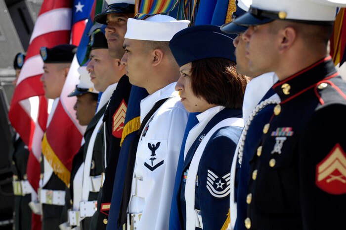 Uniformed service members from various branches stand in formation with flags.