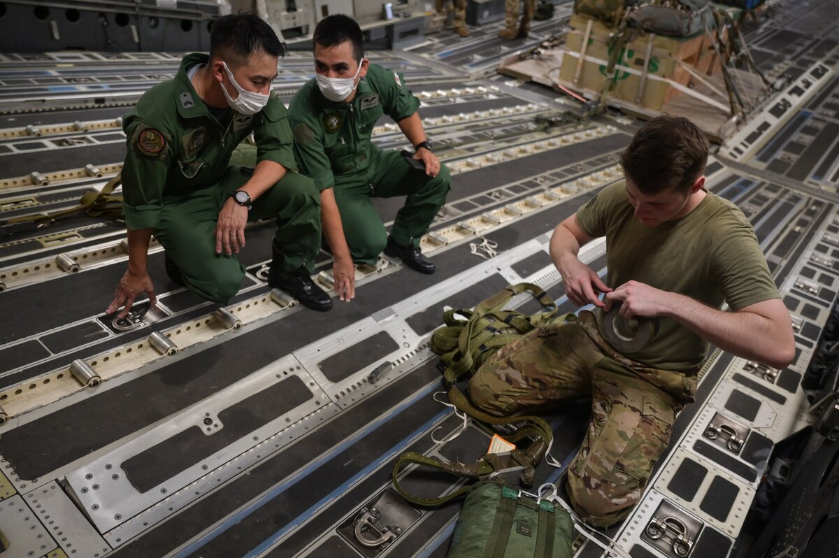 U.S. Air Force Senior Airman Andrew Girard, 535th Airlift Squadron loadmaster, secures a parachute inside a C-17 Globemaster III alongside Japan Air Self-Defense Force Senior Master Sgt. Kotaro Tanaka and Tech. Sgt. Katsuhiko Chikuma, 403rd Tactical Airlift Squadron loadmasters, during a bilateral exercise at Joint Base Pearl Harbor-Hickam, Hawaii, Sept. 28, 2022. The 3-day bilateral exercise familiarized aircrew from both services on the capabilities of the Kawasaki C-2 and the C-17. (U.S. Air Force photo by Staff Sgt. Alan Ricker)
