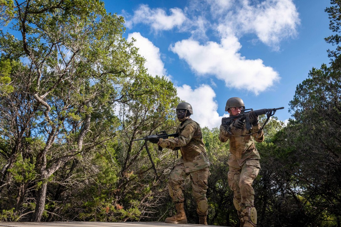 Two Air Force trainees move through the woods while carrying weapons.